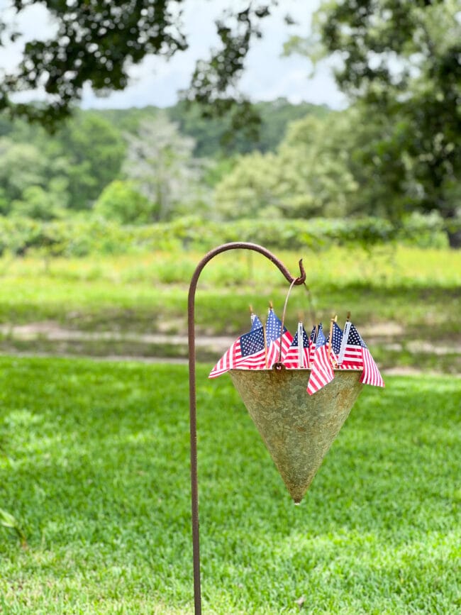 A Shepherds hook with an antique fireman's cone bucket with flags inside