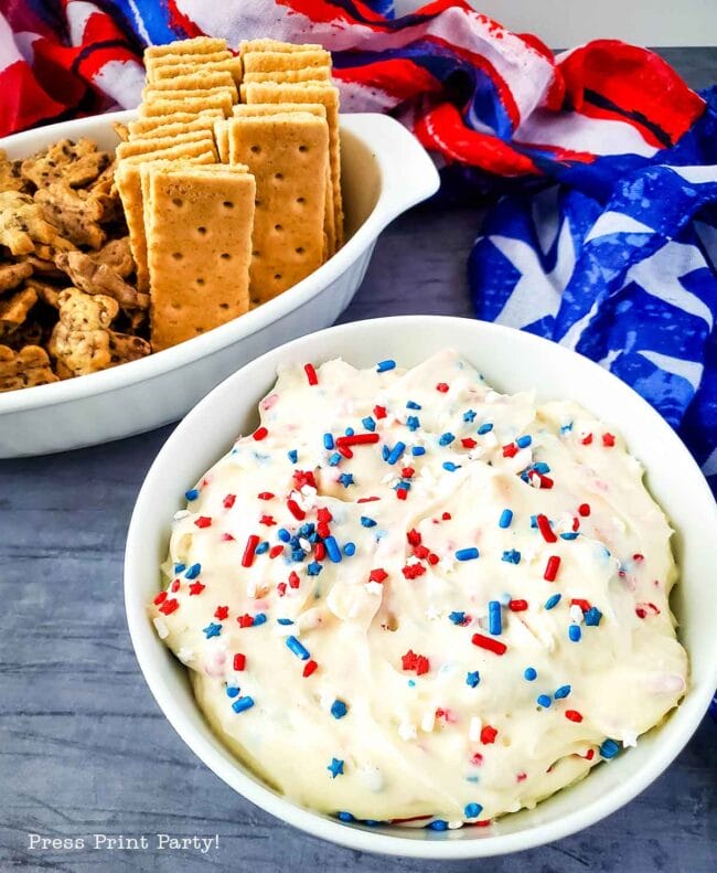 white dip with blue and red sprinkles and graham crackers in a white bowl