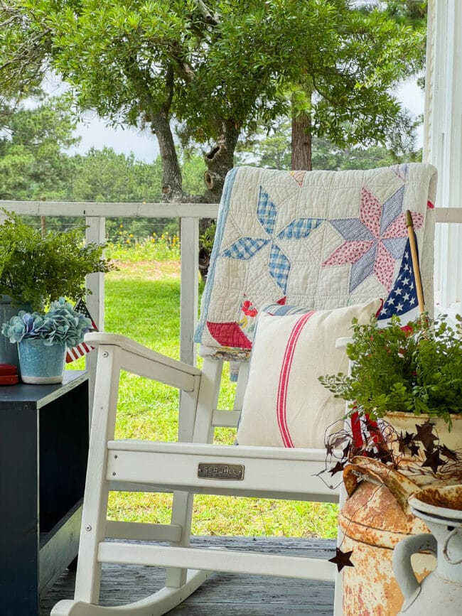 close up of a rocking chair with a quilt and pillow in red, white, and blues outside on a porch