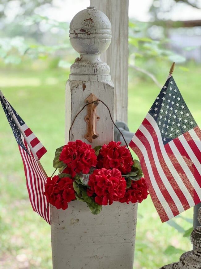 Vintage white column with 2 flags and red flowers hanging on it.