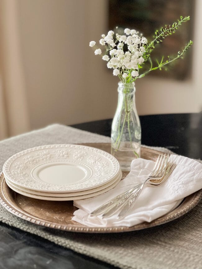 silver platter with white dishes, napkins, flowers in a bottle, and silverware