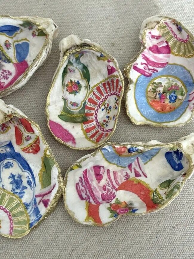 several oyster shells with decoupaged colorful papers and gold trim sitting on a fabric
