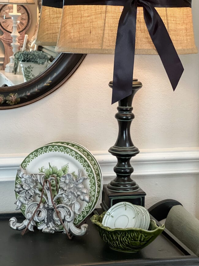 black lamp base with standing green and white plates and a leaf bowl holding vintage butter pats. 