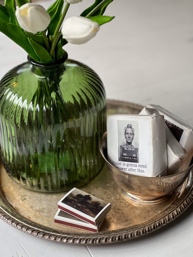 green vase with white tulips, funny soaps with faces and a stack of matches sitting on a silver tray