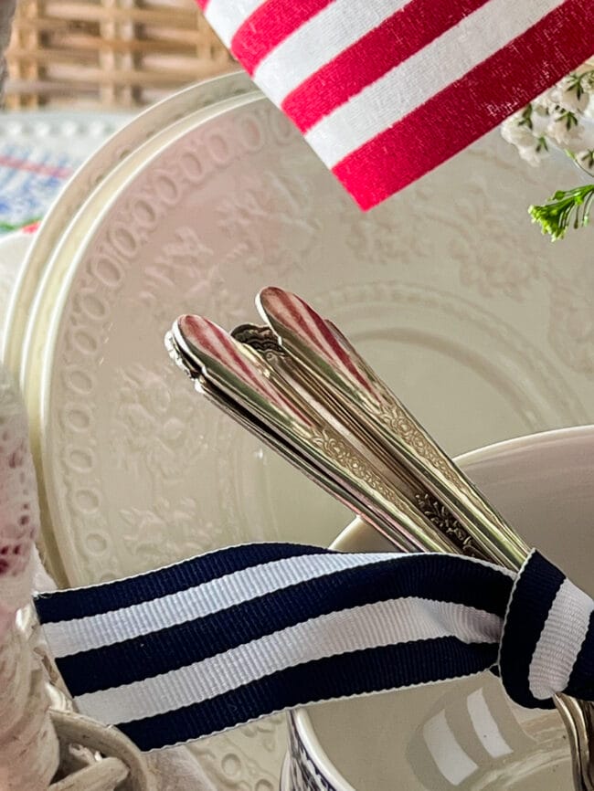 white vintage dishes stacked together with silverware tied up with blue and white striped ribbon