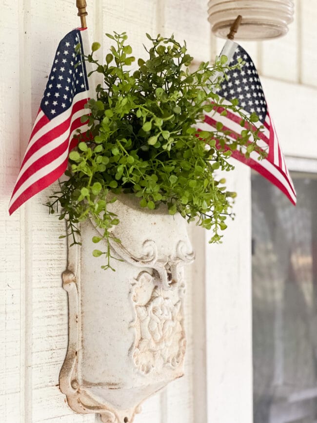 cream colored vintage cast iron mailbox with faux greenery and two US flags