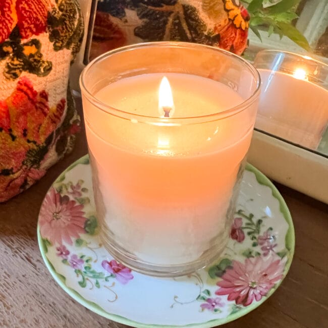 close up image of a white candle sitting in a vintage saucer with pink and green flowers