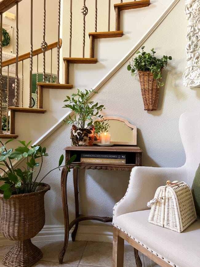 sitting area in front of stairs with a neutral chair, vintage wooden table and plants all around
