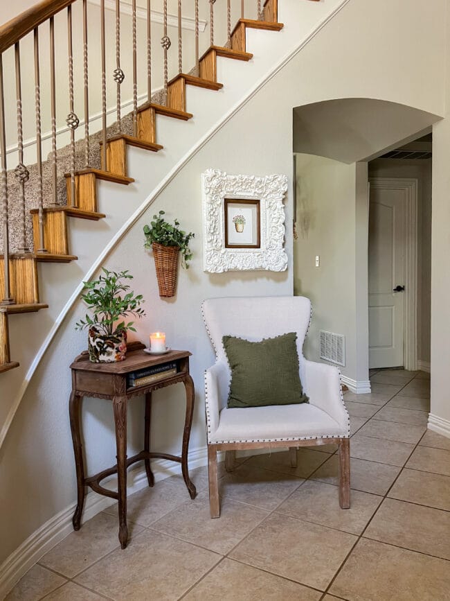 entryway with a chair, vintage table, wall art, greenery and a candle