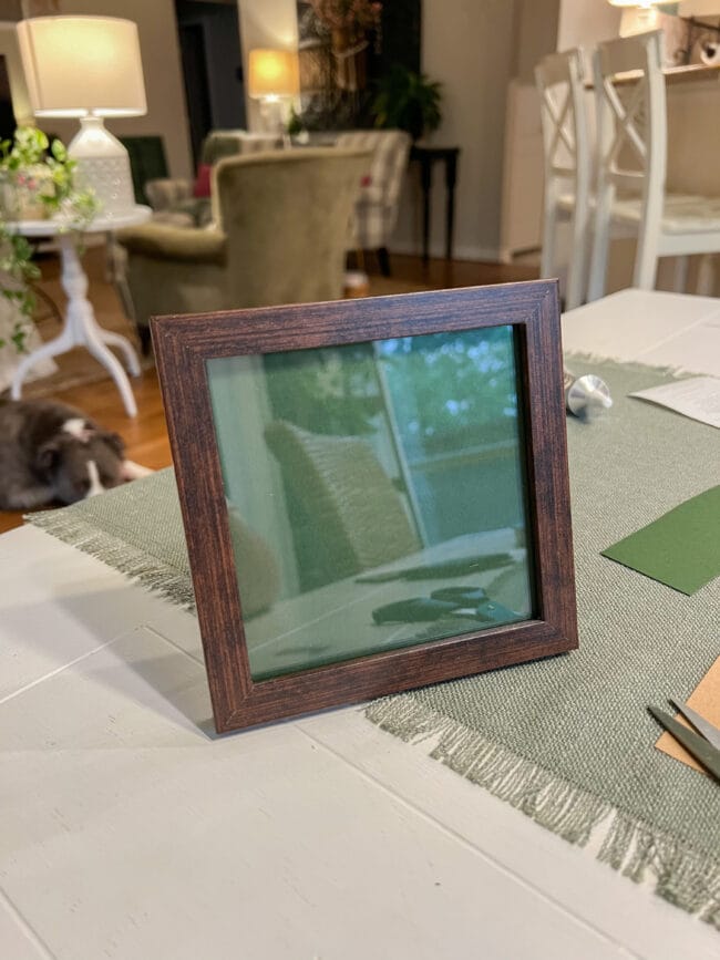 square brown 5 x 5 frame with green paper behind the glass sitting on a table
