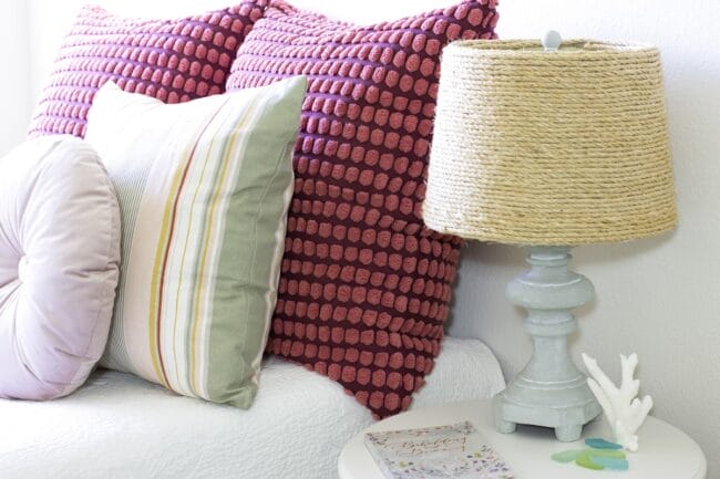red and stiped pillows with a light blue lamp and a woven shade sitting on a table
