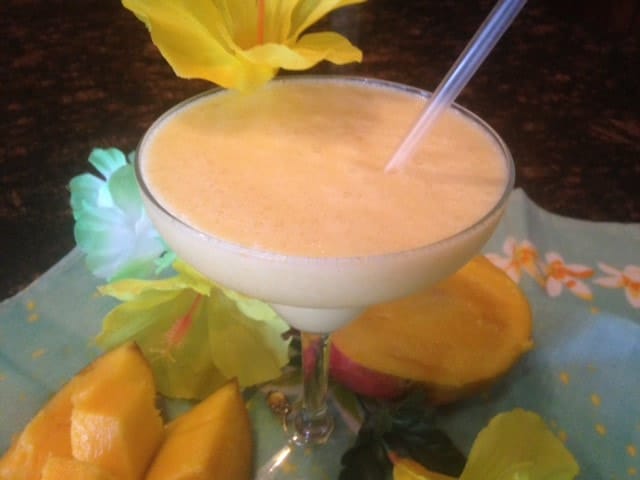 peach colored mango pineapple frozen daiquiri in a glass with a straw