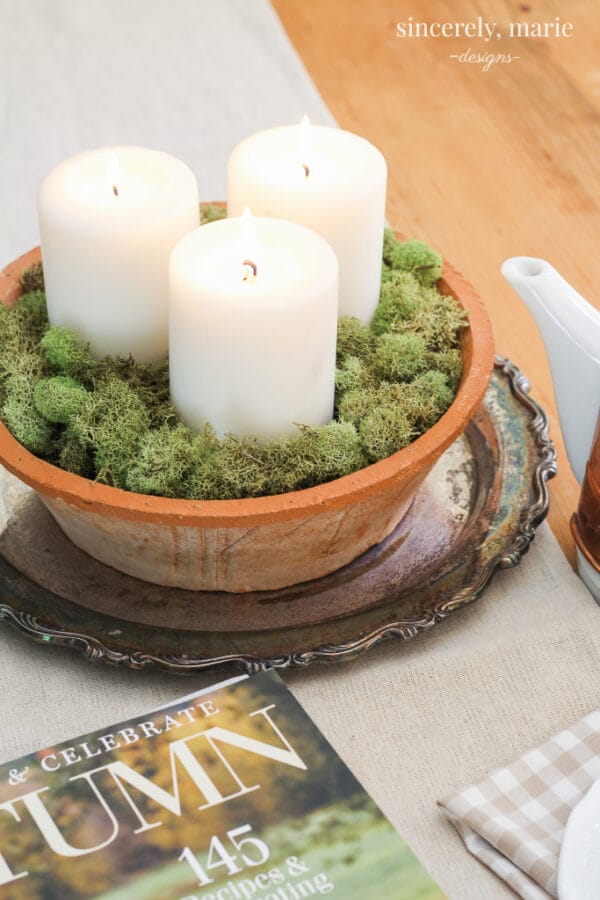 silver tray with a clay pot, white candles and moss inside sitting on a table