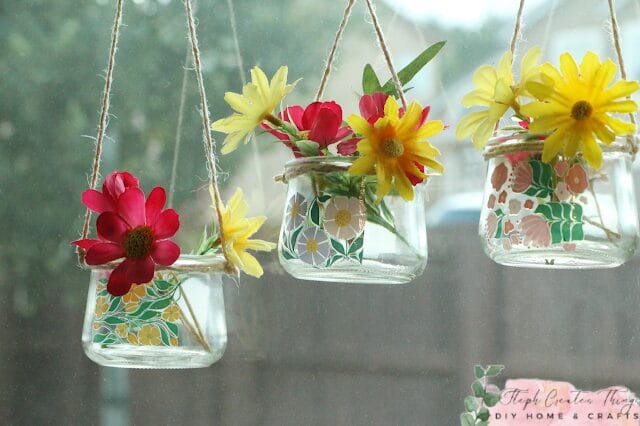 glass containers hanging in a window with flowers inside them