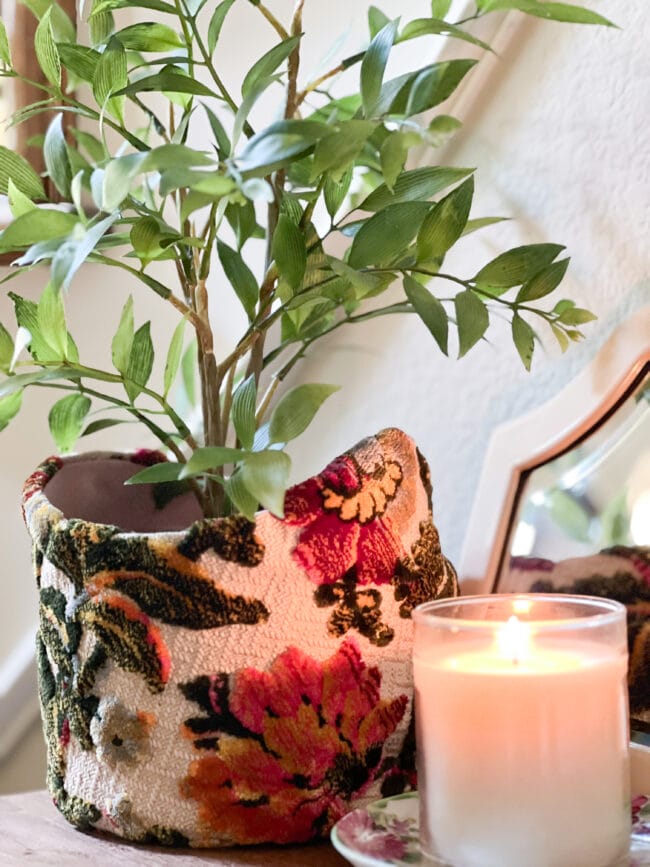 close up image of a vintage hat in a floral tapestry with a plant inside and a white candle