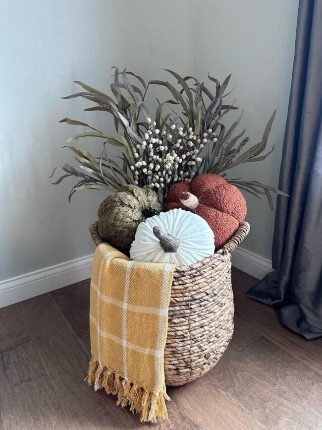 woven basket filled with a plaid blanket, pumpkins and faux stems for fall