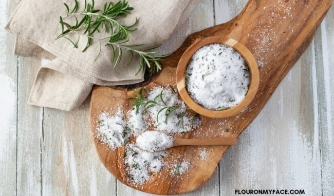 wooden board with rosemary salt, bowl and spoon sitting on top