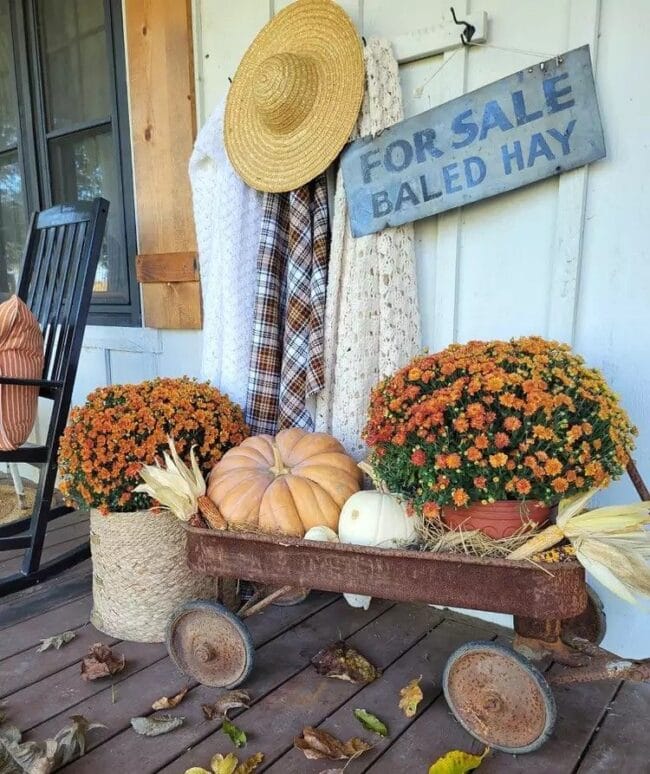 rusty wagon filled with an orange mum, pumpkins and a mum inside a crock sitting next to it.