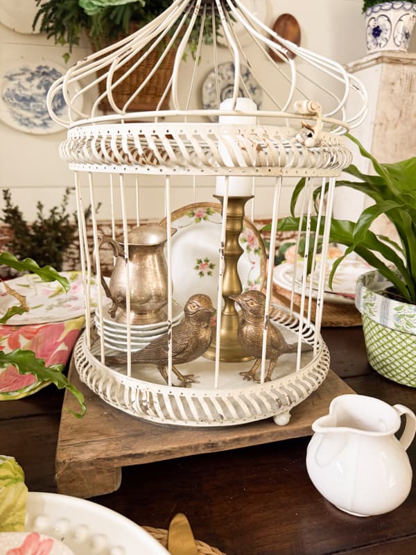 white faux birdcage with brass birds and candlestick inside. Sitting on a table