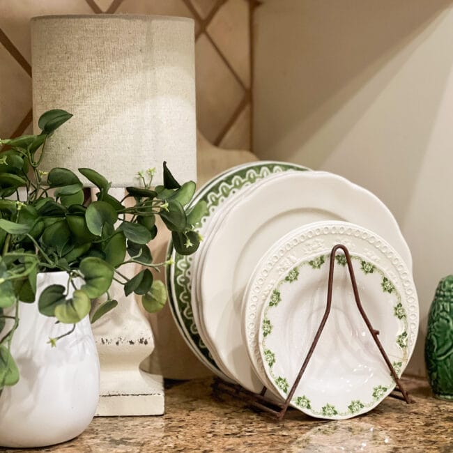 white and green dishes standing in a vintage rack with a faux plant and lamp