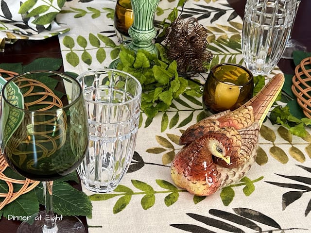 leafy table runner with green glass, a candle and finch sitting on a table setting