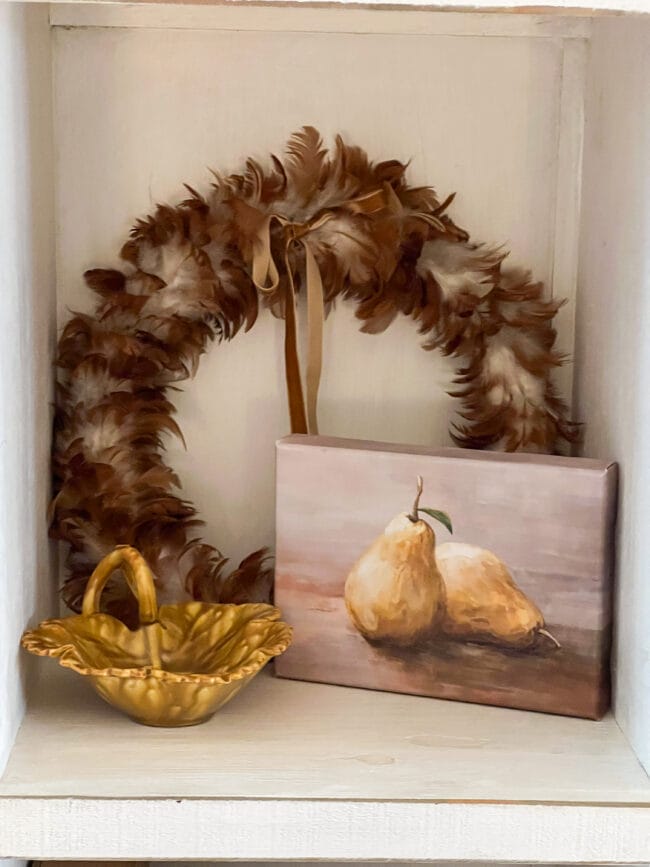 feather wreath with bow, gold leaf shaped plate and a pear canvas sitting together