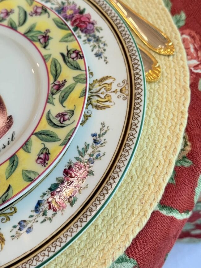 yellow placemat with two floral antique plates with gold and silver flatware on a red floral tablecloth