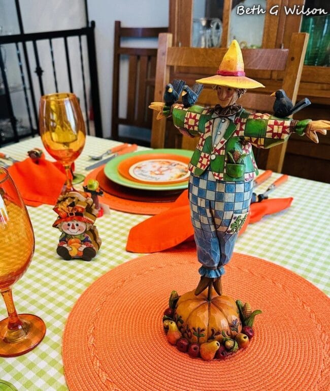 green and orange tablescape with scarecrow centerpiece and gold glasses