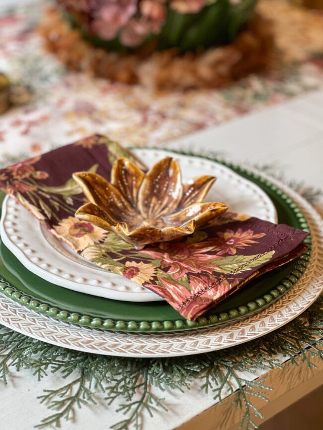 place setting with green plates, white salad plate, fall napkin and gold floral shaped bowl on top