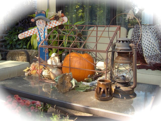 outdoor cage with scarecrow, orange pumpkin and a lantern sitting on a table