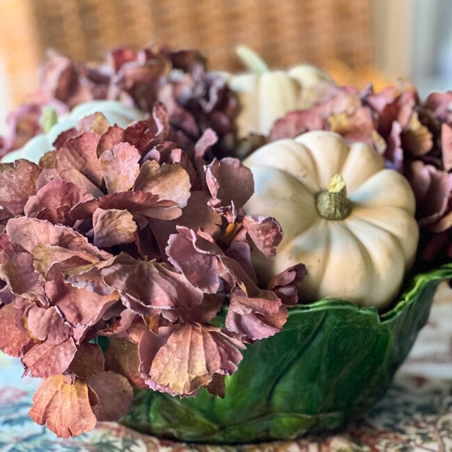 Green lettuce bowl with purple faux flowers and white pumpkins