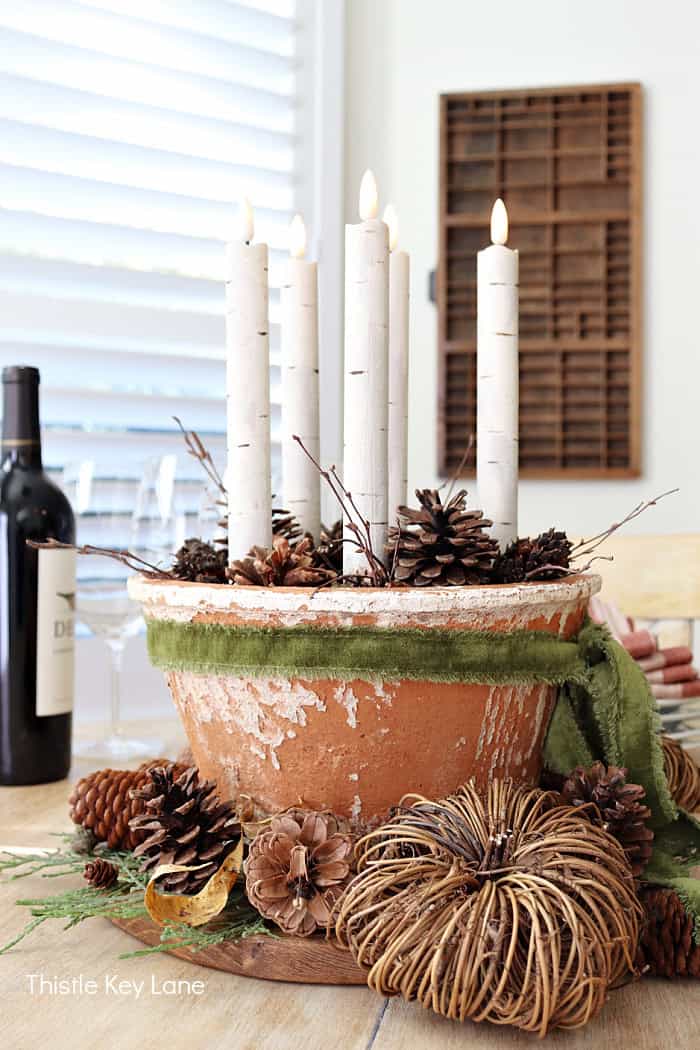worn terracotta pot on a table with pinecones and white candles