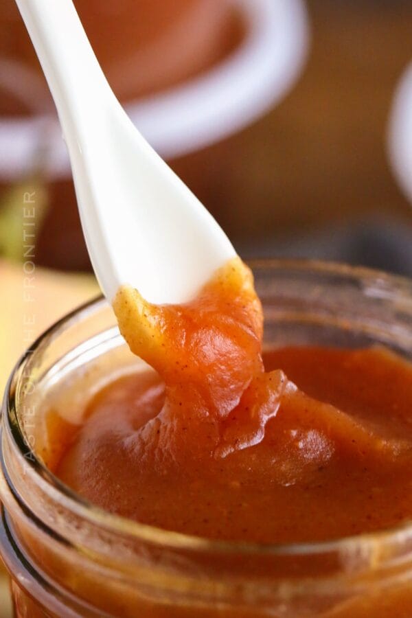 close up of apple butter on the end of a white spoon dipped in a jar