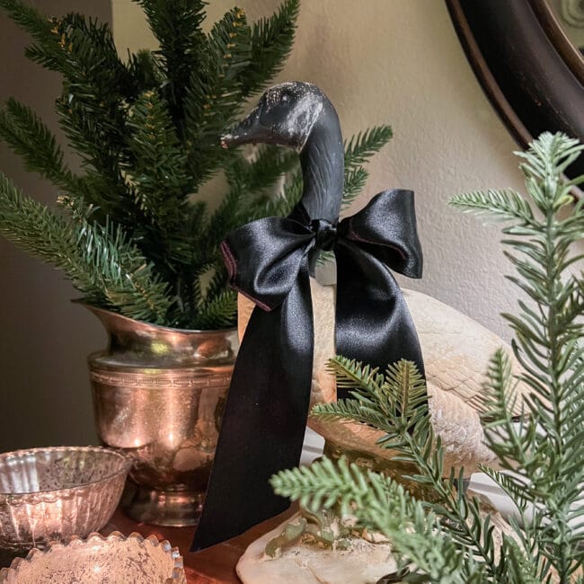 green Christmas trees in silver pots, a ceramic goose with a black ribbon tied around its neck and lit candles in vintage candy dishes