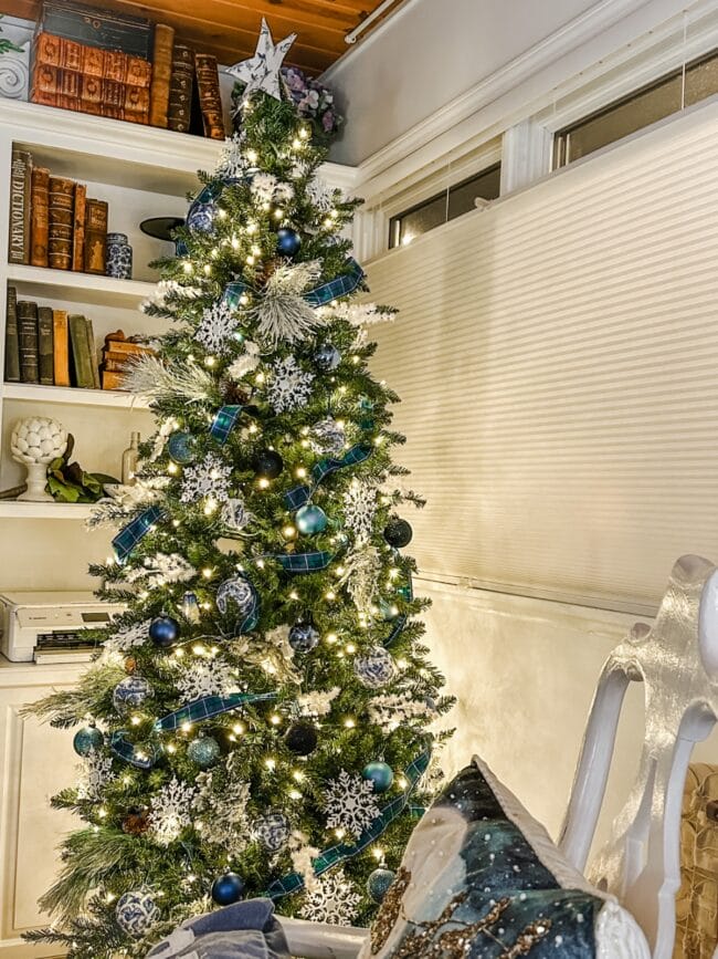 blue and white decorated Christmas tree with a bookshelf in the background