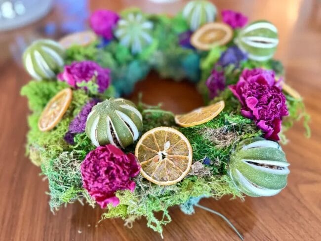 wreath made with green moss, citrus fruit pieces, and fuchsia flowers