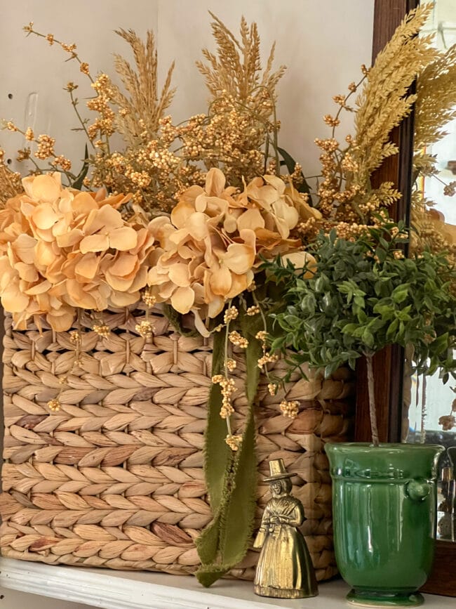 straw basket with gold flowers and stems, a small topiary in a green pot with a brass pilgrim bell
