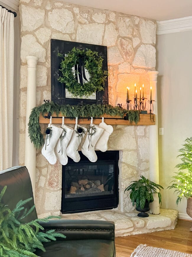 close up view of stone fireplace, black mirror and wreath on mantel and white stockings 