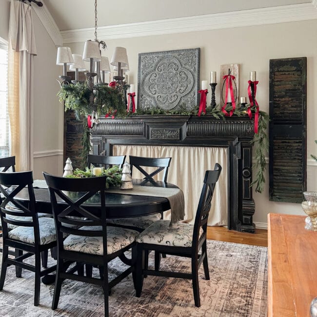 Full dining room with black mantel with shutters on either side, black dining table and candles on mantel with red bows