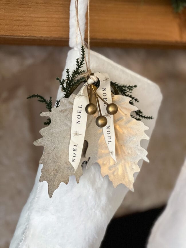 white stocking with two gold metal leaves, a noel ribbon and metal berries