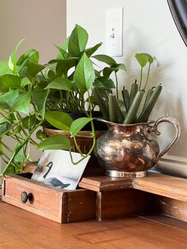 ivy plant with a goose print and a silver creamer with green candles inside