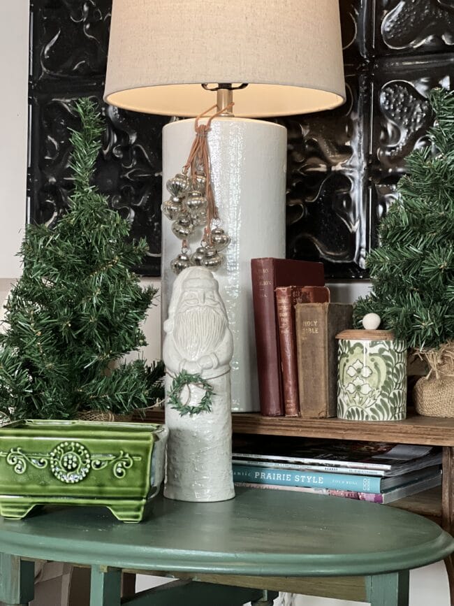 white ceramic santa with small wreath, books, and two small trees
