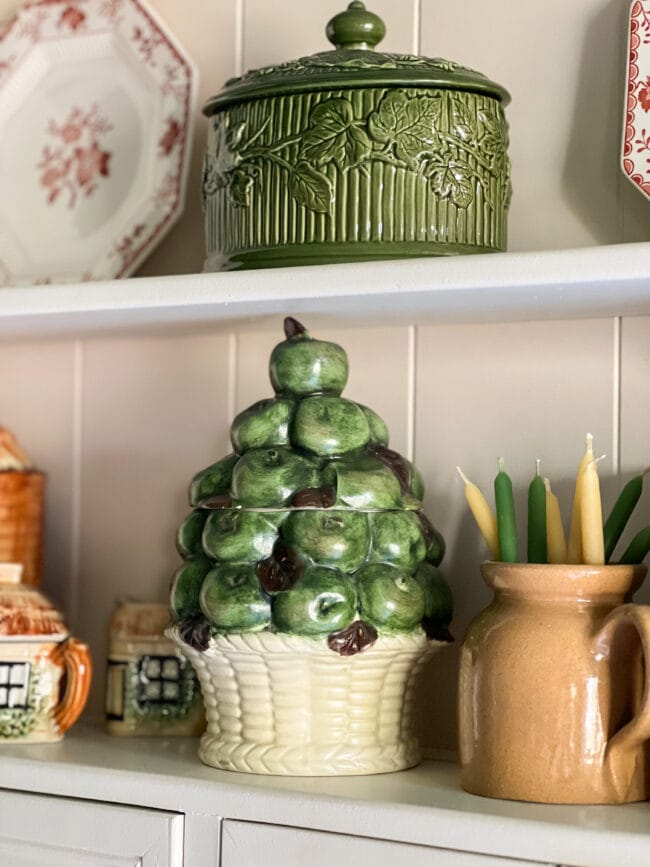 small green apple canister sitting on shelf with other small fall colored pottery 