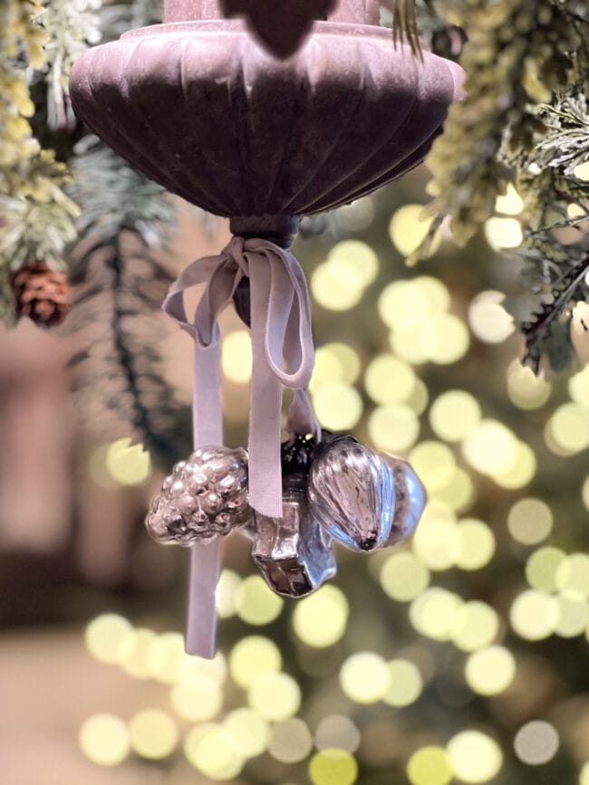 small silver ornaments hanging with a bow and lights in the background