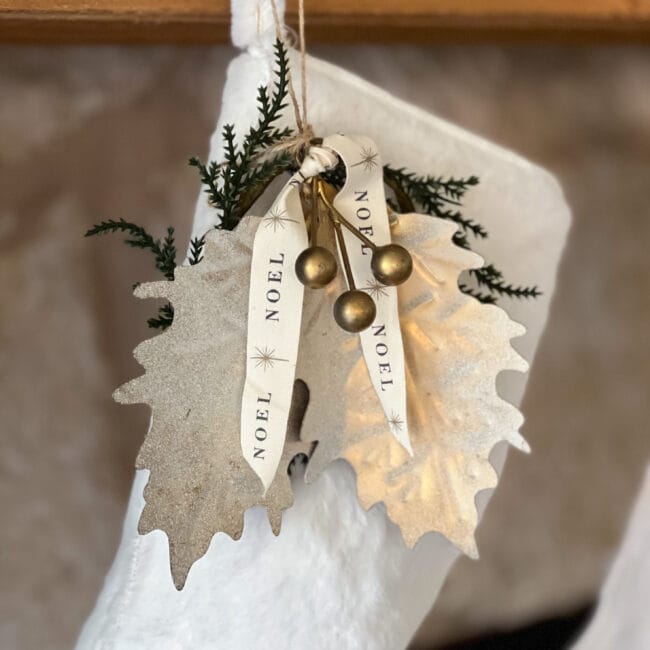 white fur stocking with gold metal leaves, gold berries and a noel ribbon tied around it.