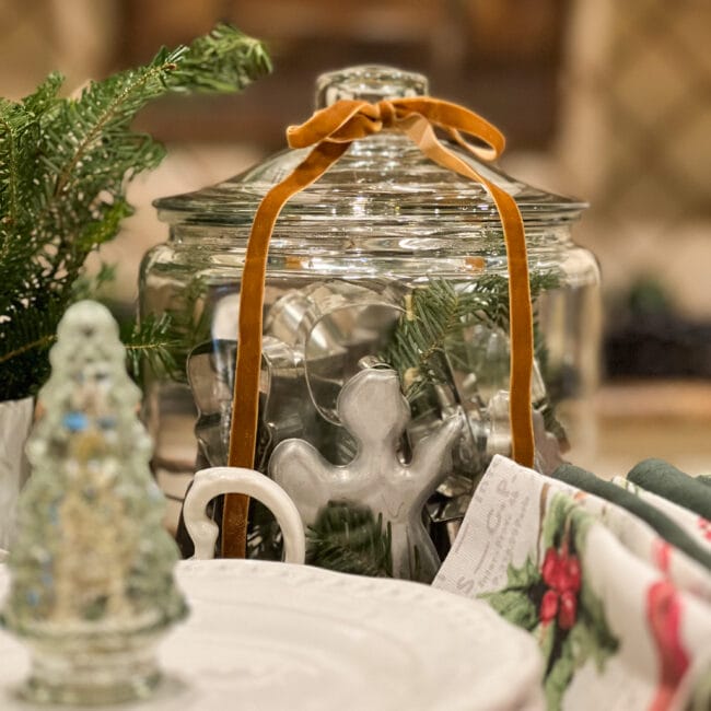 clear glass canister with vintage cookie cutters, ribbon on the lid and greenery