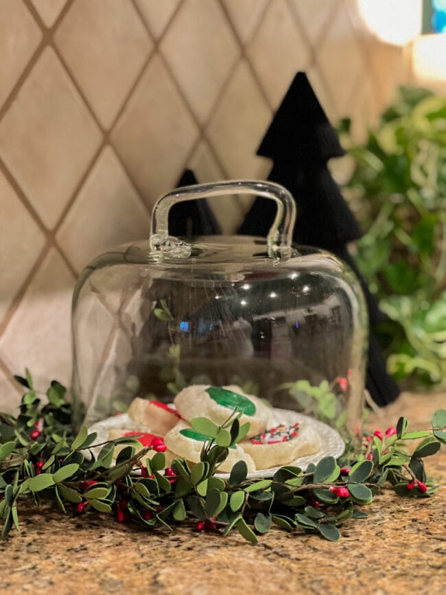 cookies under a glass cloche with a wreath around the bottom.