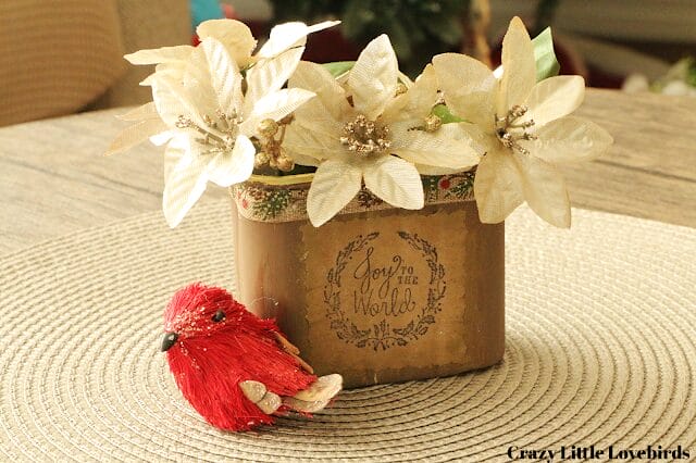 Christmas box with white faux flowers and a little red bird sitting in front of it.