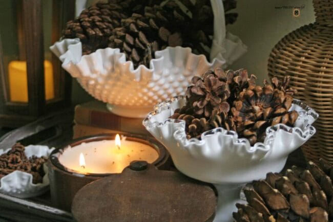 white milk glass candy dishes with pinecones for winter decorating and a lit candle