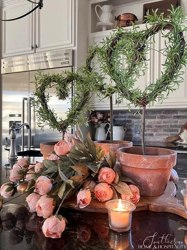 3 heart shaped topiaries with pink roses and a candle on a kitchen counter